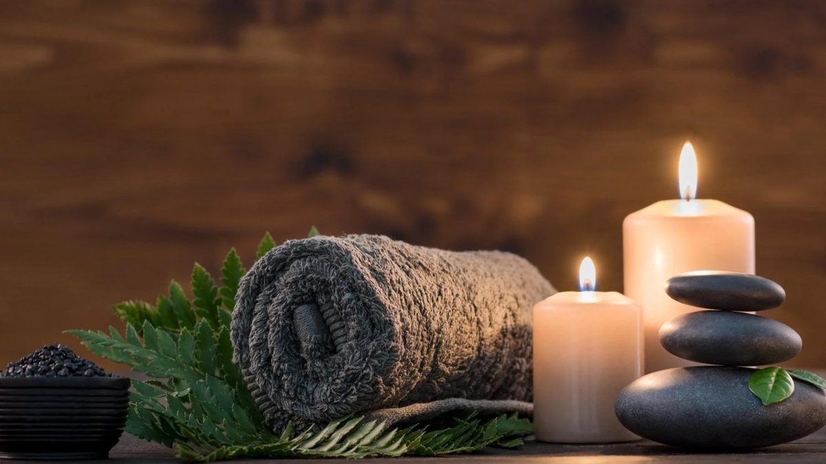 Ambiente de spa neutro con toalla enrollada, velas encendidas y piedras lisas apiladas, sin personas